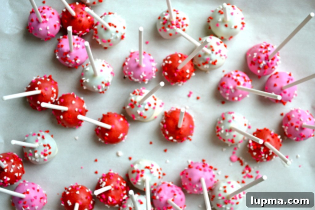 Stuck on Sweet: Valentine's Day Oreo Cake Pops 3 Several festive Oreo cake pops decorated with red, pink, and white sprinkles, arranged on a Valentine's Day themed backdrop.