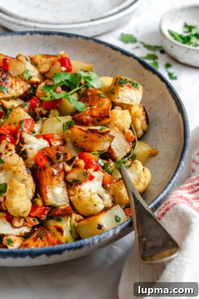 Creamy Cauliflower Potato Salad 4 A close-up of Cauliflower Potato Salad in a white bowl, showing the texture and vibrant colors of the roasted vegetables, peppers, and almonds