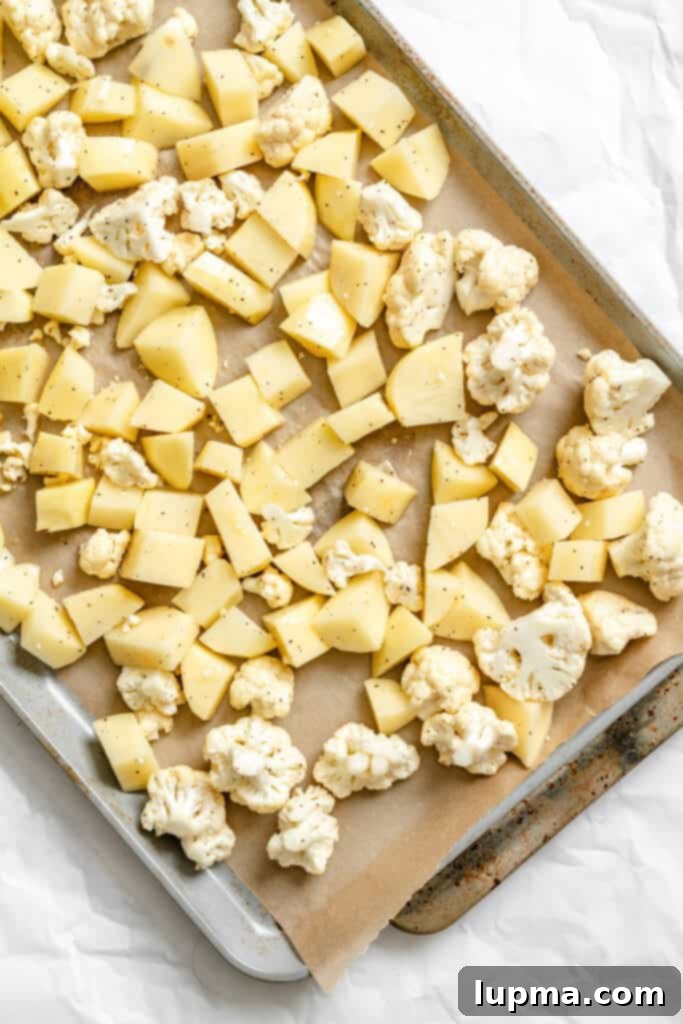 Creamy Cauliflower Potato Salad 6 Cauliflower and potato pieces spread on a baking sheet, ready for roasting, seasoned with olive oil, salt, and pepper