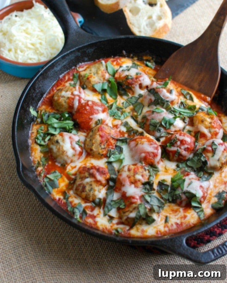 Garden Fresh Skillet Tomato Basil Meatballs 2 A skillet filled with warm, cheesy tomato basil meatballs, garnished with fresh basil, ready to be served with baguette slices.