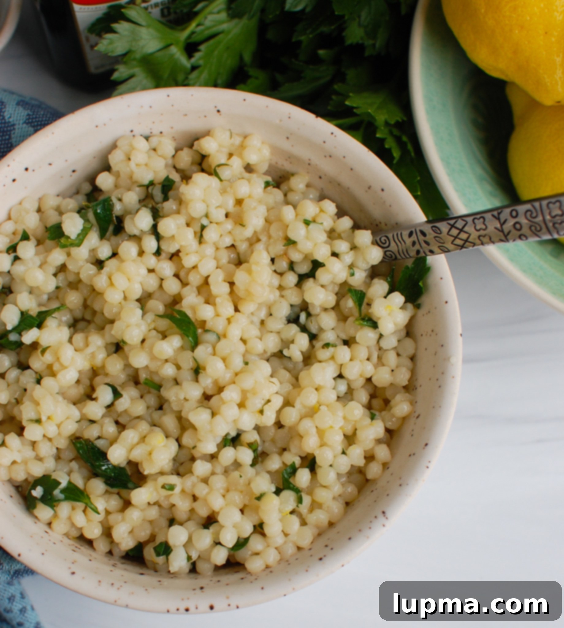 Bright Lemon Pearl Couscous Creations 4 Close-up of Lemon Pearl Couscous Recipe in a bowl with a serving spoon, highlighting the lemon and herbs.