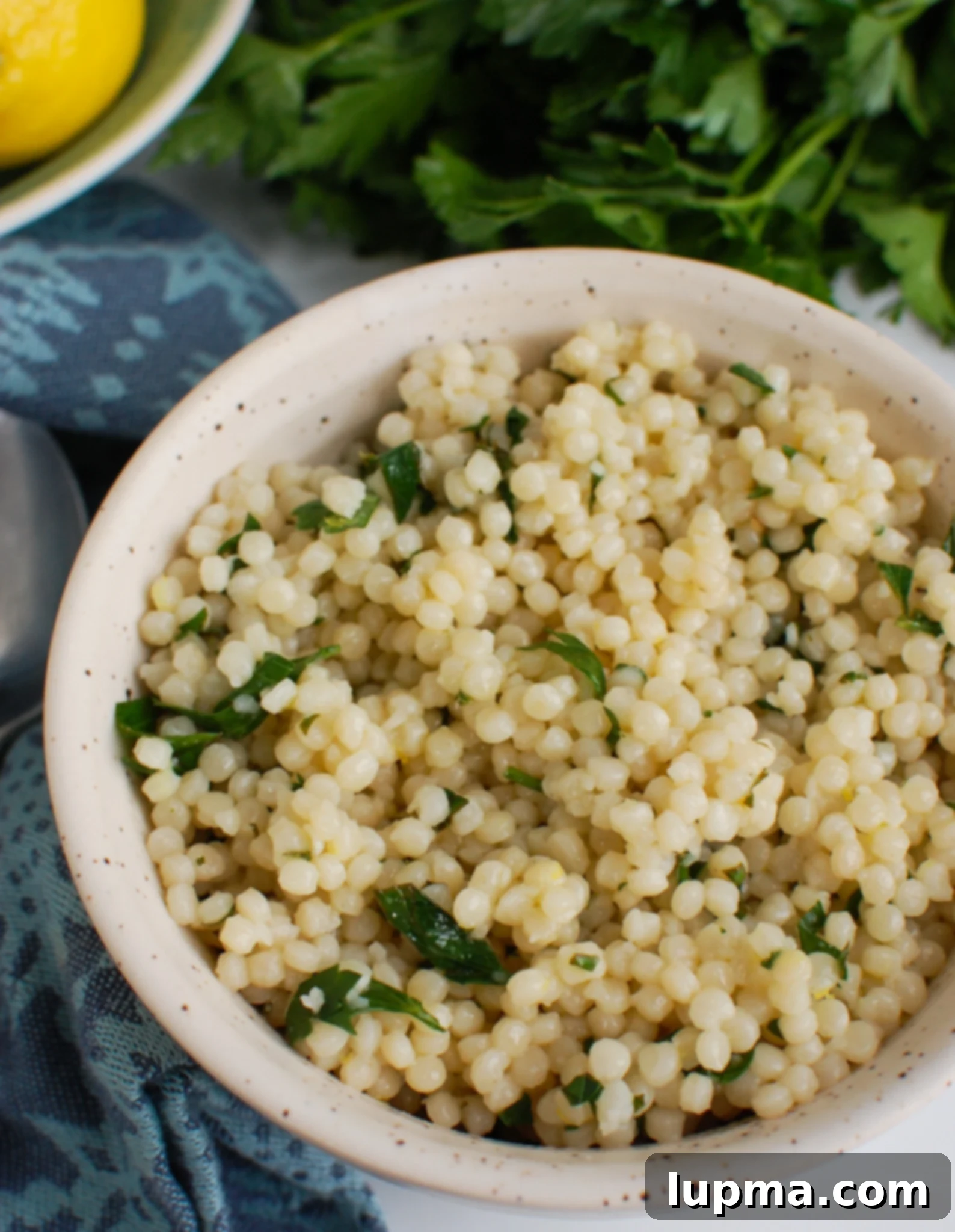Bright Lemon Pearl Couscous Creations 6 A bowl of Lemon Pearl Couscous Recipe placed on a wooden board with a napkin, ready to be served.