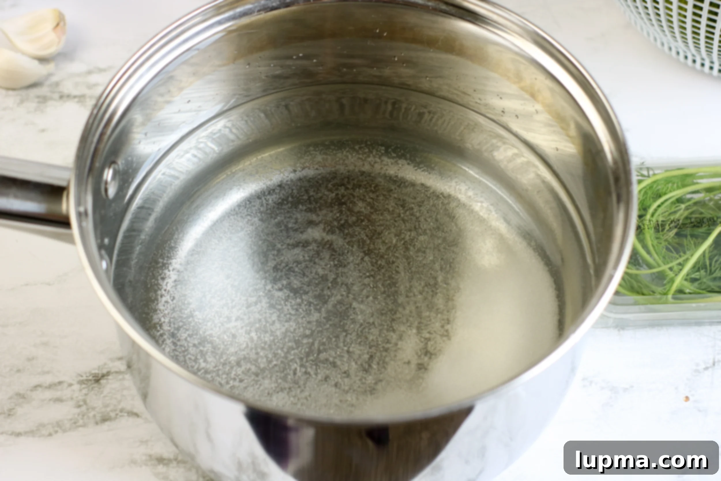 Speedy Refrigerator Dill Pickles 6 A pickling brine mixture boiling in a saucepan on a stovetop, indicating the first step of preparing Refrigerator Dill Pickles.