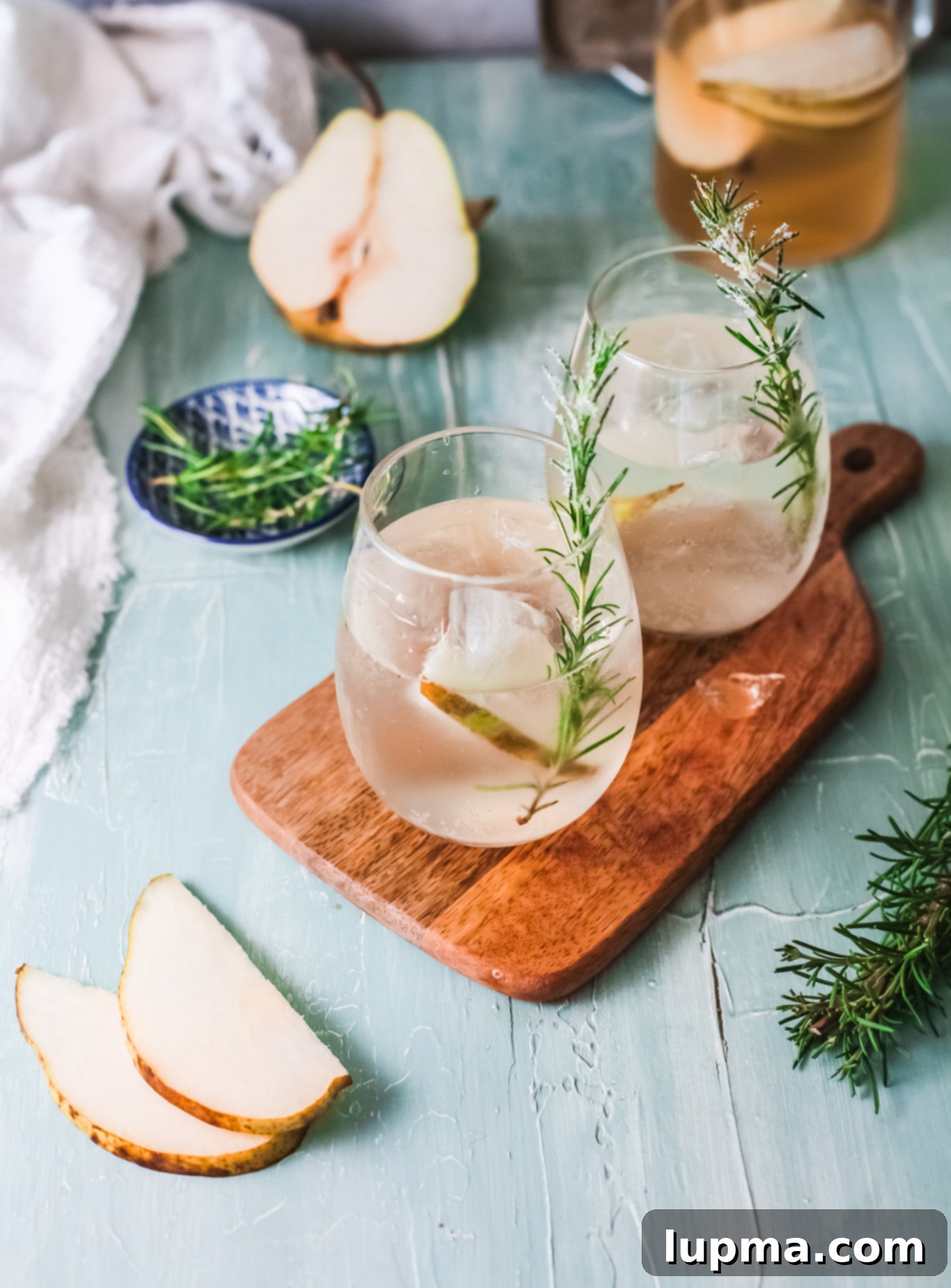 Effortlessly Delicious White Sangria 2 White Sangria Recipe in a glass, garnished with pear slices and rosemary, sitting on a rustic wooden surface.