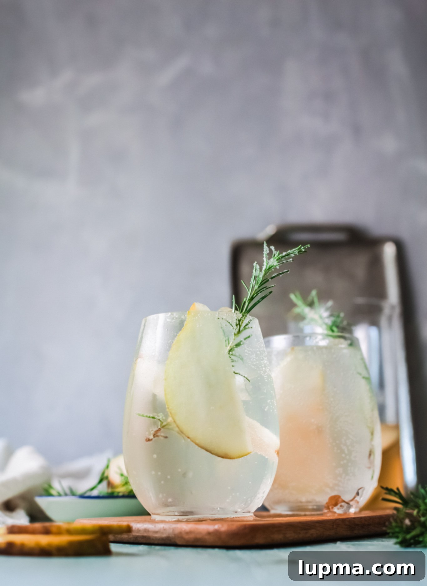 Effortlessly Delicious White Sangria 3 A tall glass of White Sangria Recipe with rosemary and pear slices, sparkling with ice cubes.