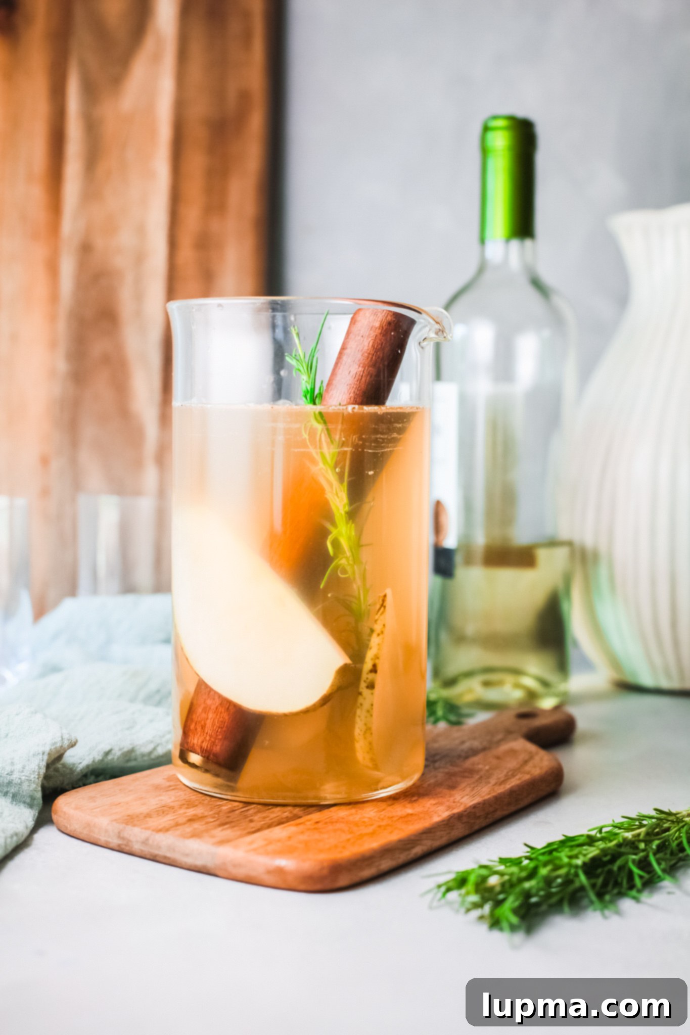 Effortlessly Delicious White Sangria 4 White Sangria Recipe being poured into a pitcher with fruit and rosemary.