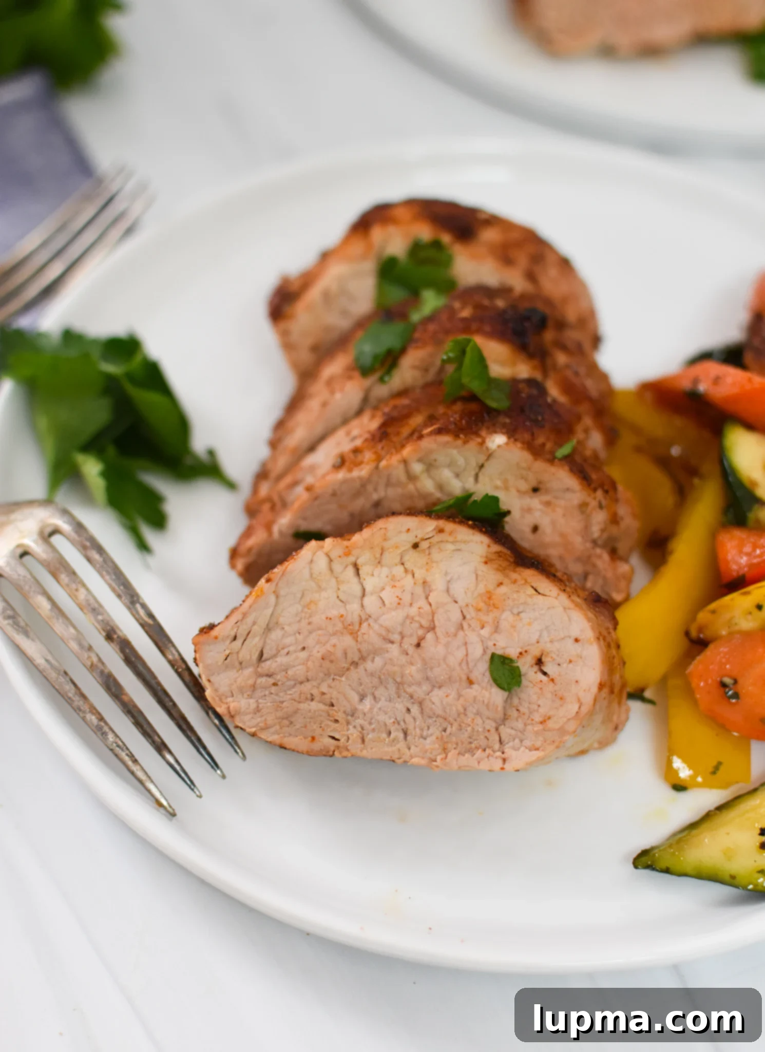 Juicy Air Fryer Pork Tenderloin 2 Air Fryer Pork Tenderloin on a white plate with a fork, ready to be enjoyed.