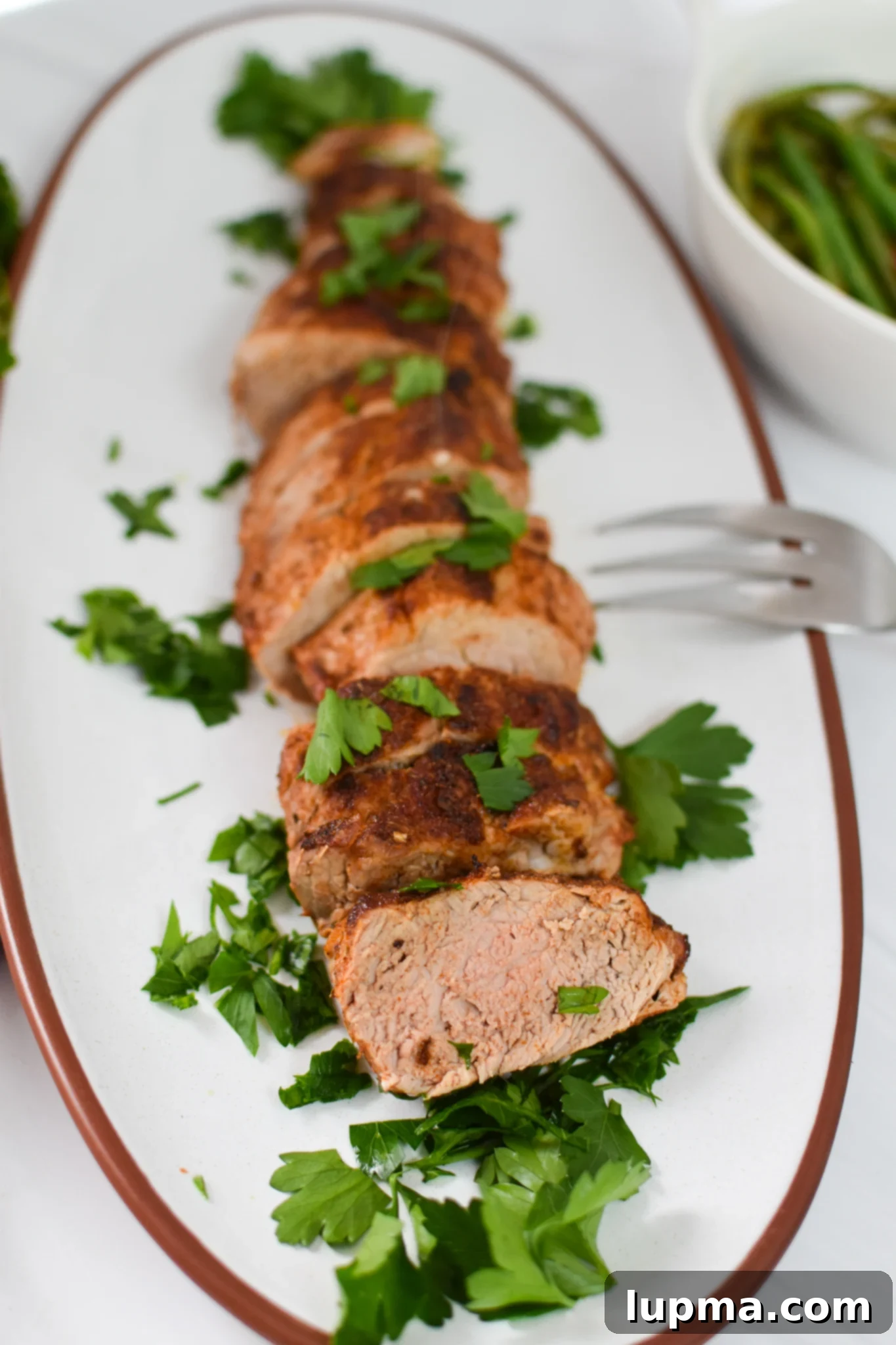 Juicy Air Fryer Pork Tenderloin 4 Air Fryer Pork Tenderloin on a white platter, perfectly cooked and ready to slice.