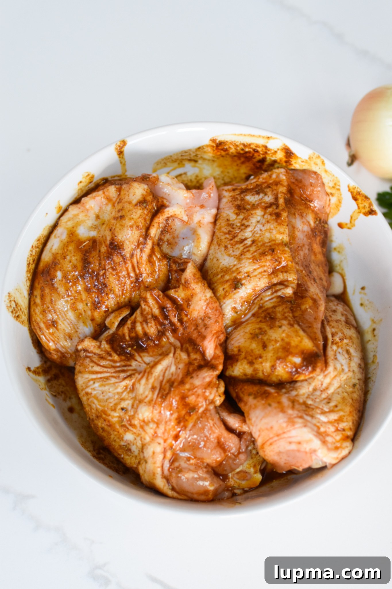 Sun-Kissed Mediterranean Chicken & Rice 5 Marinating chicken thighs in a bowl with Mediterranean spices for the One Pot Mediterranean Chicken and Rice recipe.
