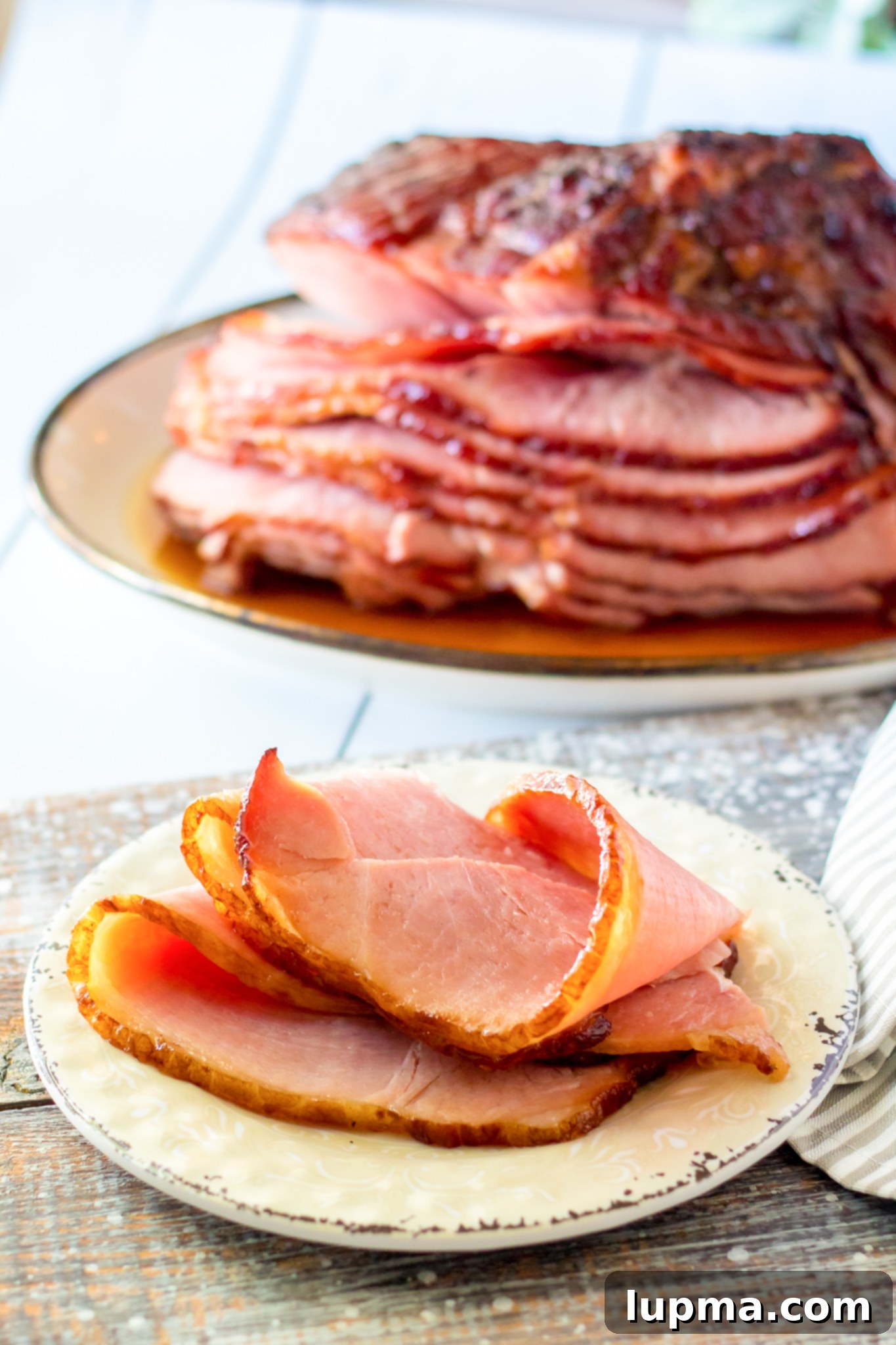Sweet and Sticky Apple Cider Glazed Ham 4 Close-up of a slice of Apple Cider Glazed Ham on a white plate, showing its juicy texture.