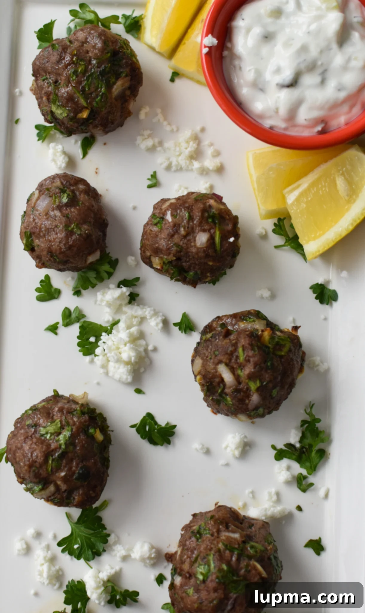 Mediterranean Golden Beef Meatballs 7 A pristine white platter filled with golden-brown Mediterranean Baked Beef Meatballs, perfectly cooked and ready to be enjoyed.