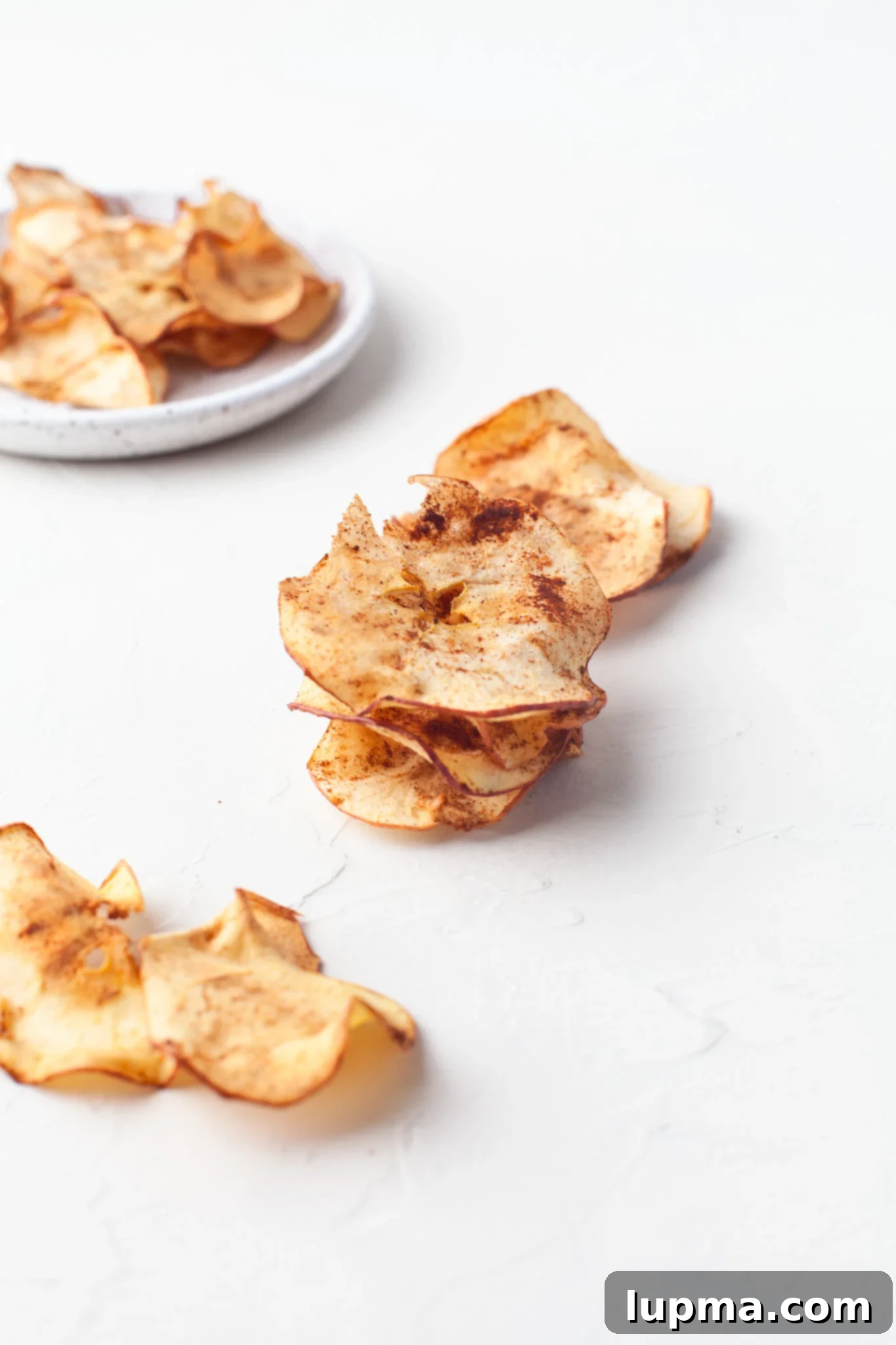 Quick & Crispy Air Fryer Apple Chips 9 Easy Air Fryer Apple Chips arranged on a white table.