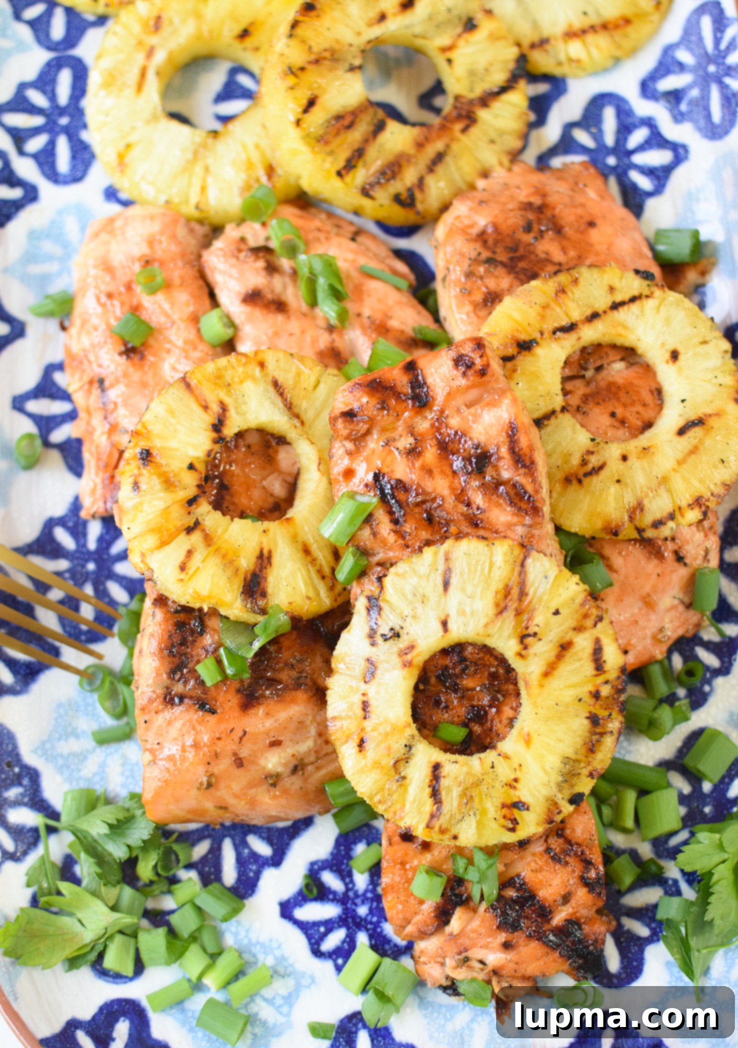 Aloha Grilled Salmon 2 Perfectly grilled Hawaiian salmon fillets and pineapple on a blue platter, garnished with fresh herbs.