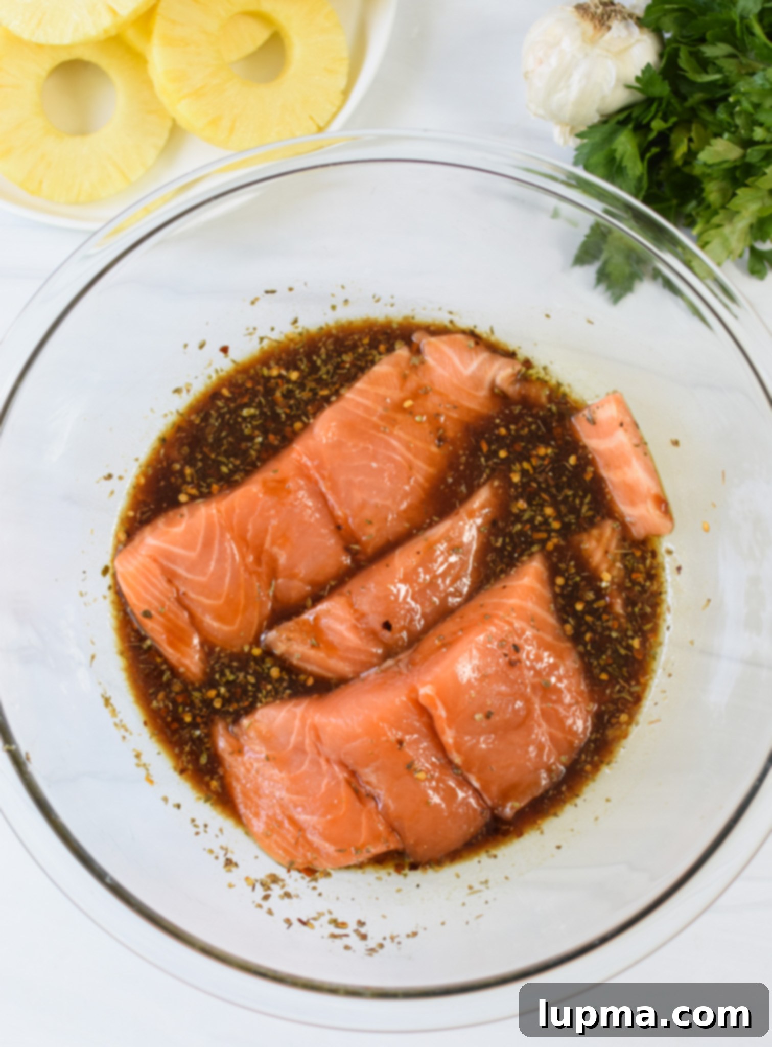 Aloha Grilled Salmon 7 Hawaiian salmon fillets marinating in a bowl, ready for grilling, with fresh pineapple slices nearby.