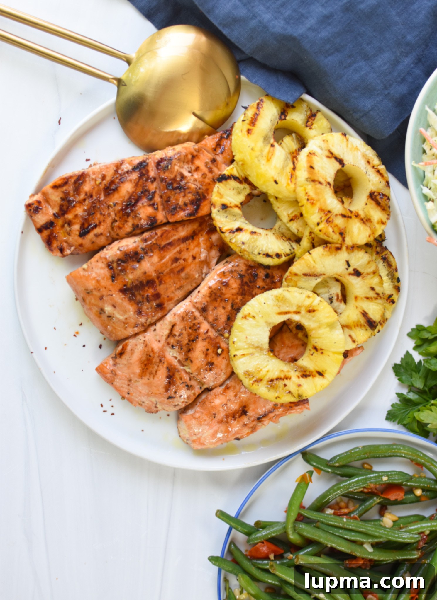 Aloha Grilled Salmon 8 A serving of Hawaiian Grilled Salmon with green beans and a wedge of grilled pineapple on a white plate.