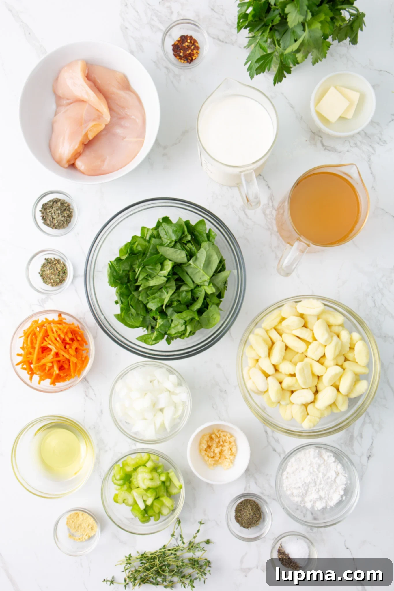 Homemade Olive Garden Style Chicken Gnocchi Soup 4 A flat lay of fresh ingredients including garlic, onion, celery, carrots, chicken breasts, spinach, and spices, laid out for Copycat Olive Garden Chicken Gnocchi Soup.