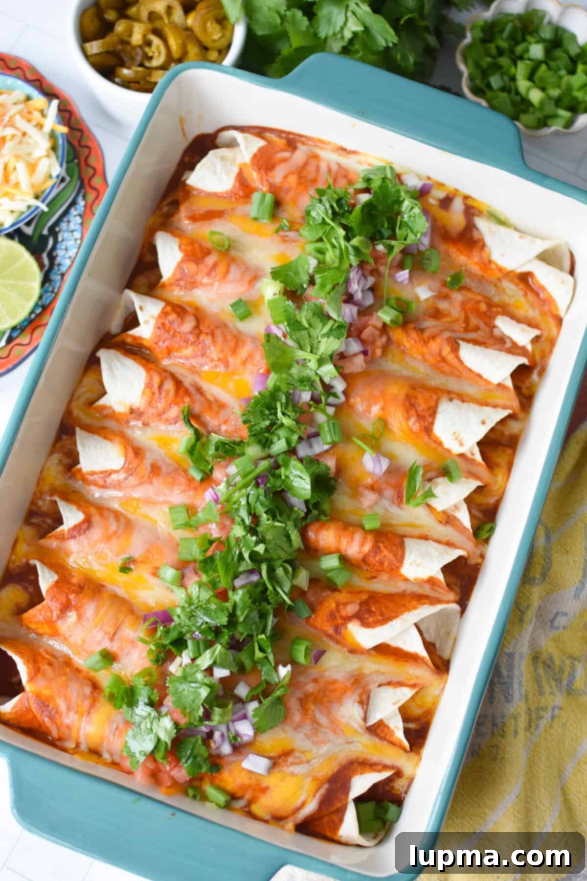 Speedy Pork Enchiladas 4 A baking dish filled with savory pork enchiladas, generously covered in melted cheese and vibrant enchilada sauce, garnished with fresh cilantro and red onions.
