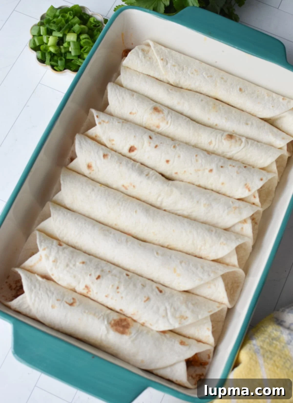 Speedy Pork Enchiladas 5 Rolled pork enchiladas placed neatly, seam-side down, in a glass casserole dish, ready for sauce and cheese.