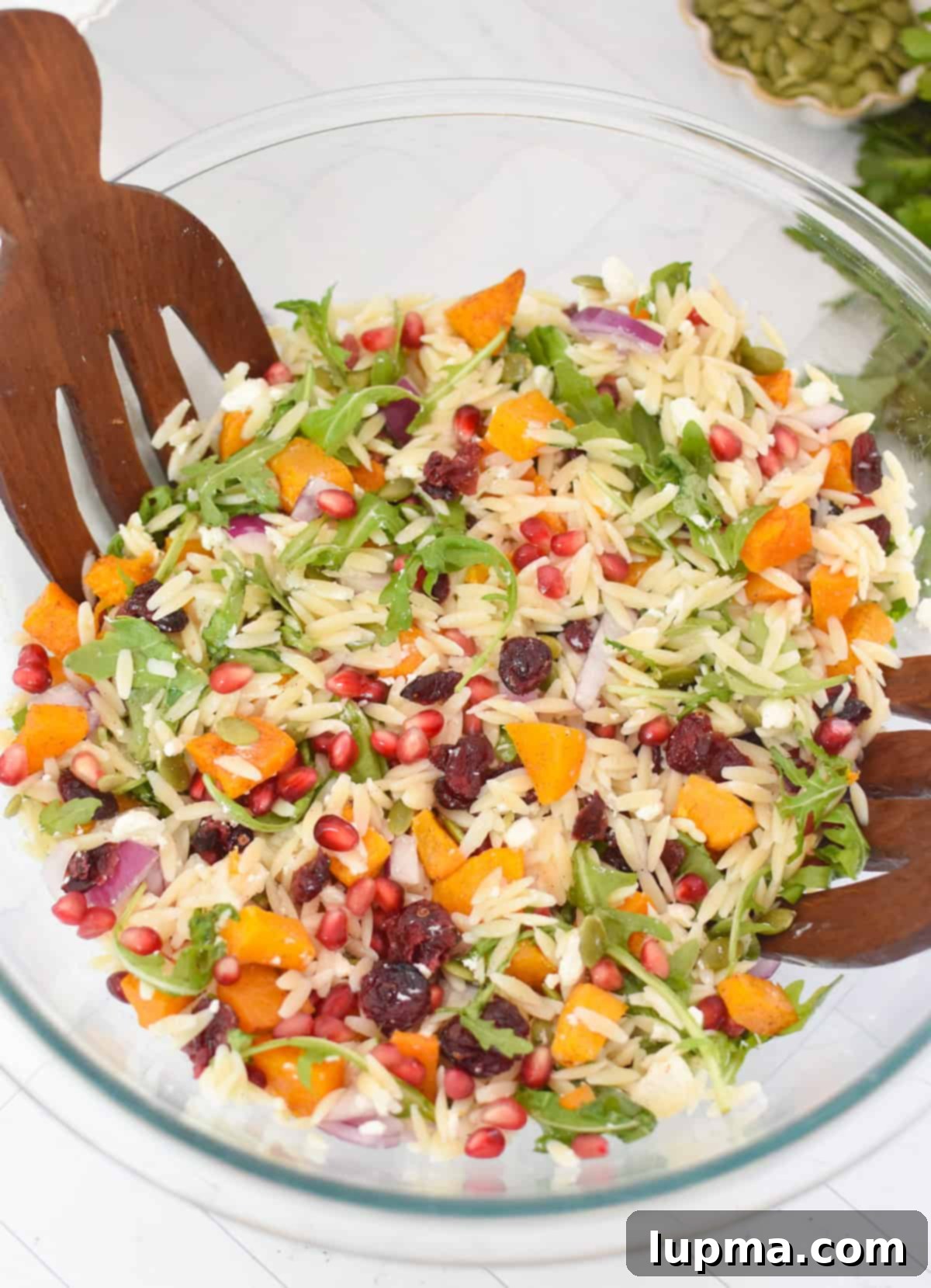 Hearty Autumn Orzo Salad 12 Fall Orzo Pasta Salad tossed with dressing in a glass bowl, with wooden serving forks.