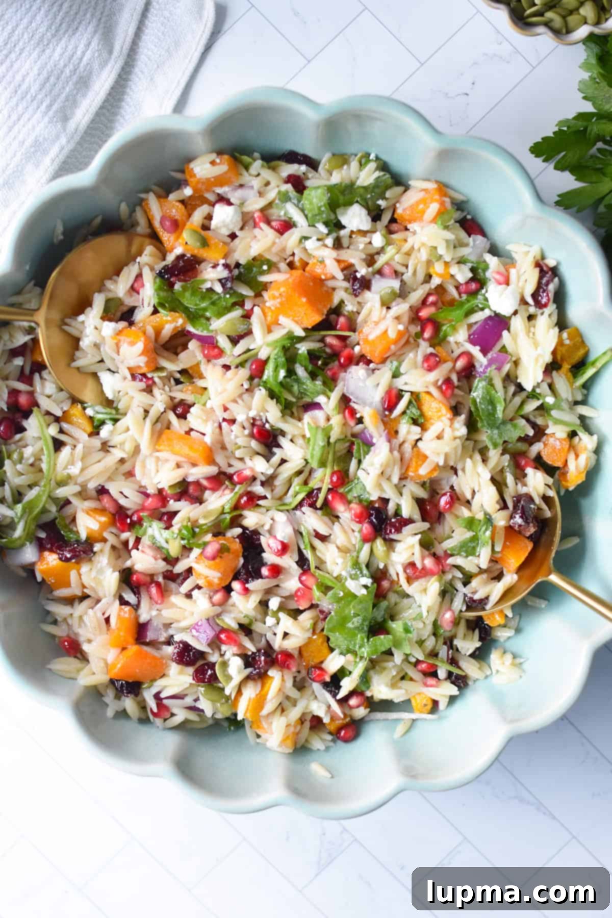 Hearty Autumn Orzo Salad 7 A large glass bowl overflowing with Fall Orzo Pasta Salad, garnished with a sprig of fresh herbs and wooden serving spoons, ready for a gathering.