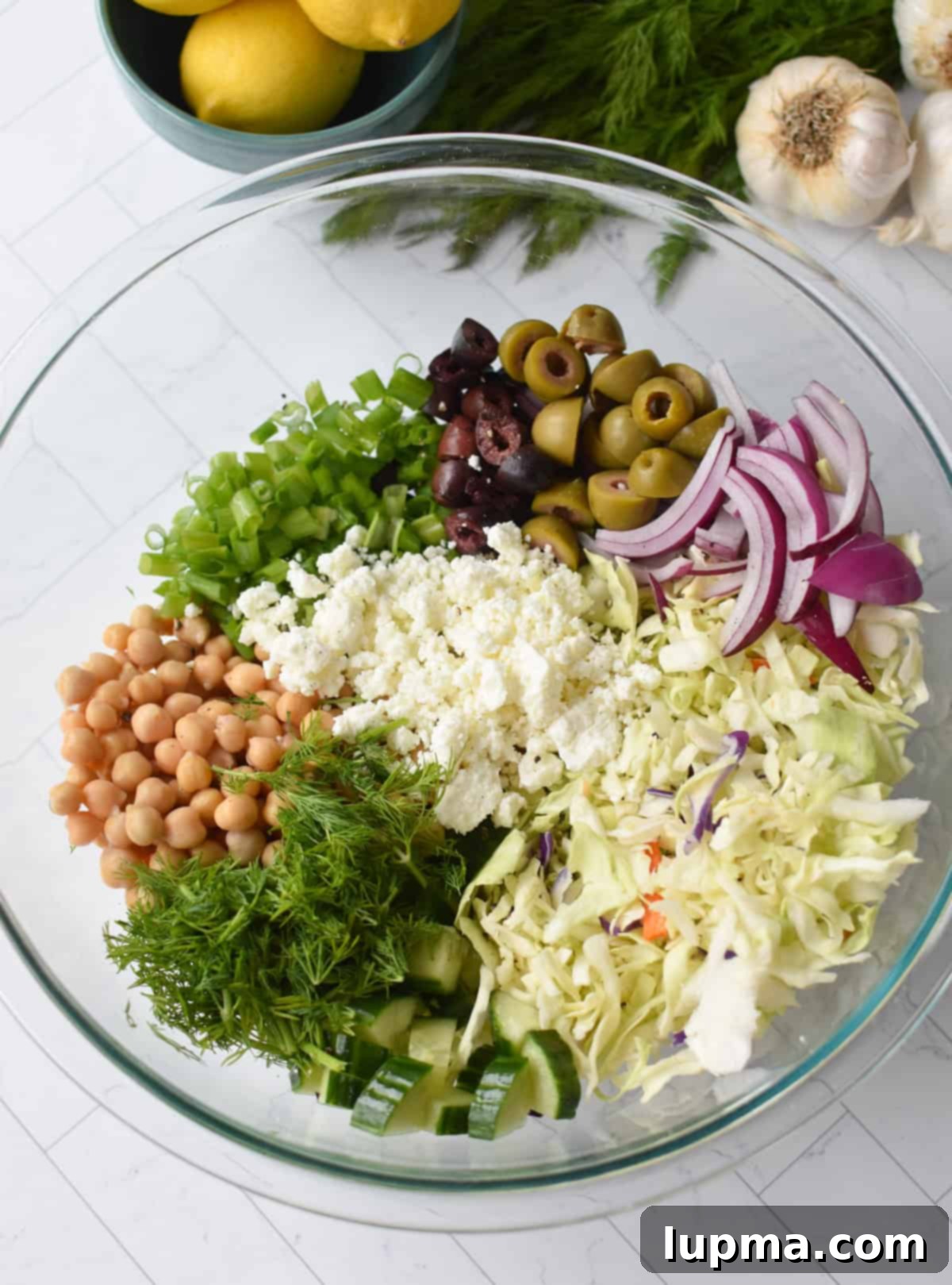 Greek Cabbage Salad ingredients pre-mixed in a large clear bowl