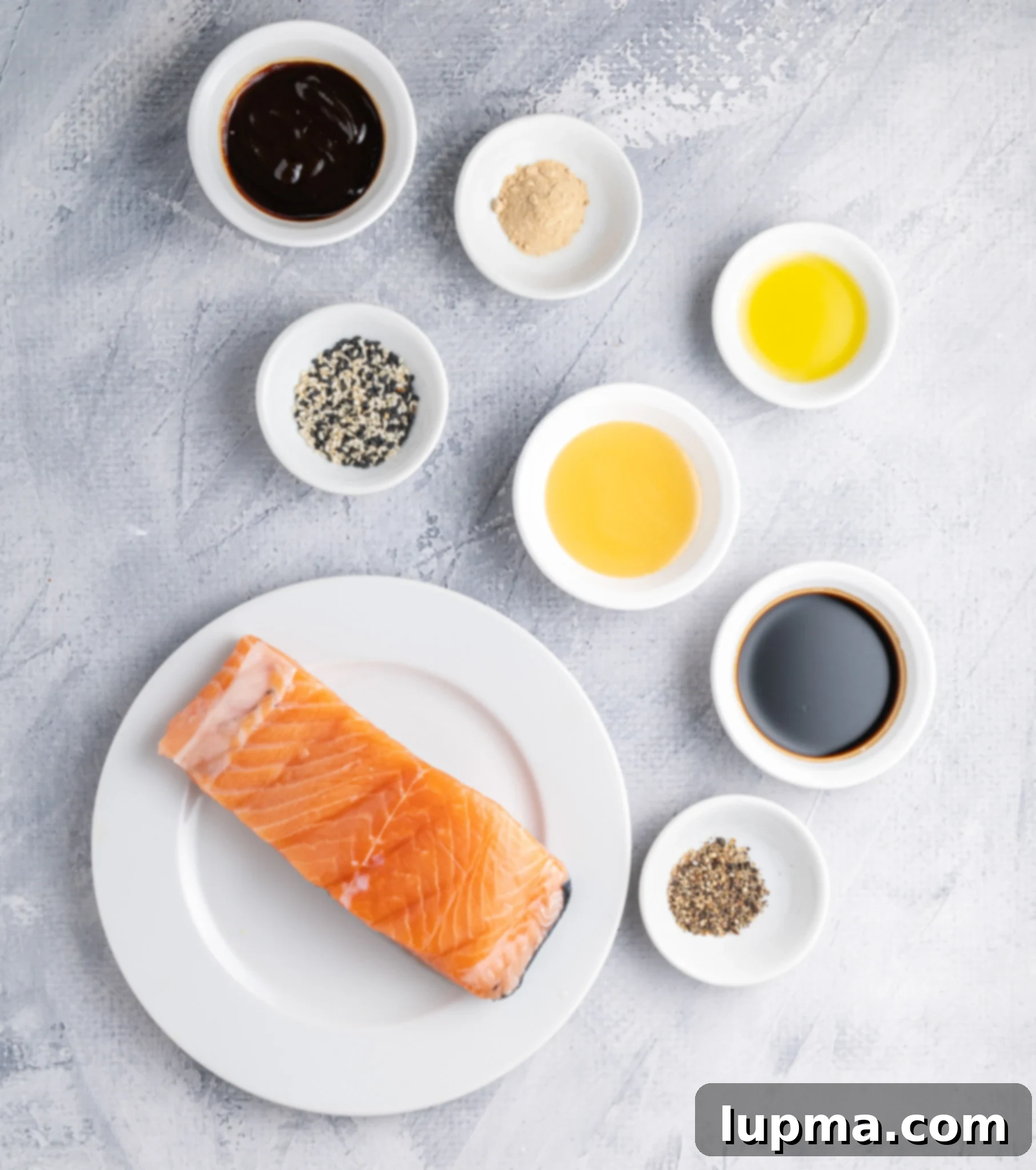 Teriyaki Salmon Bites: An Air Fryer Sensation 5 A salmon fillet on a white plate surrounded by small bowls containing various ingredients.