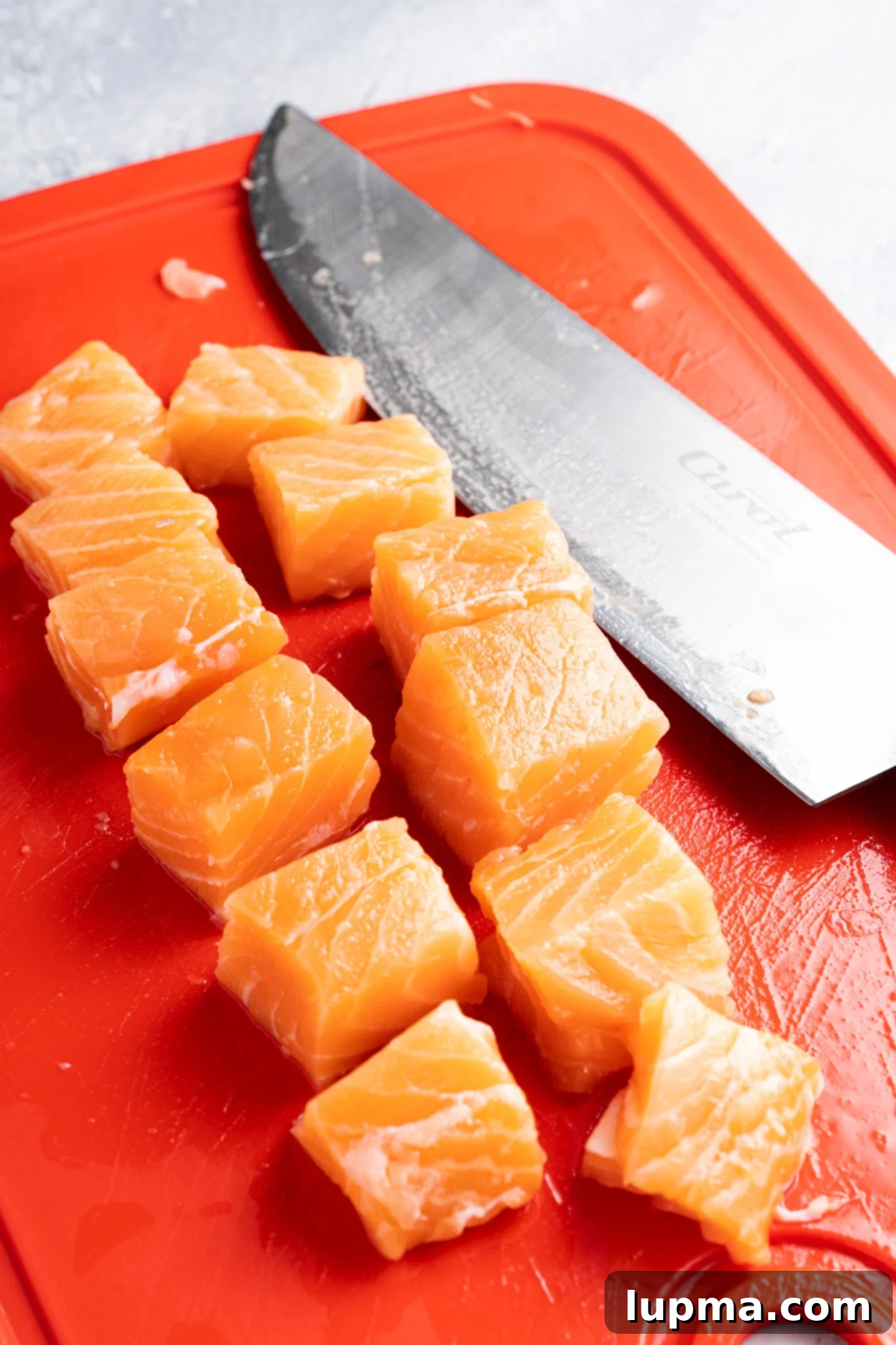 Teriyaki Salmon Bites: An Air Fryer Sensation 6 Cubes of fresh salmon are neatly arranged on a bright red cutting board.