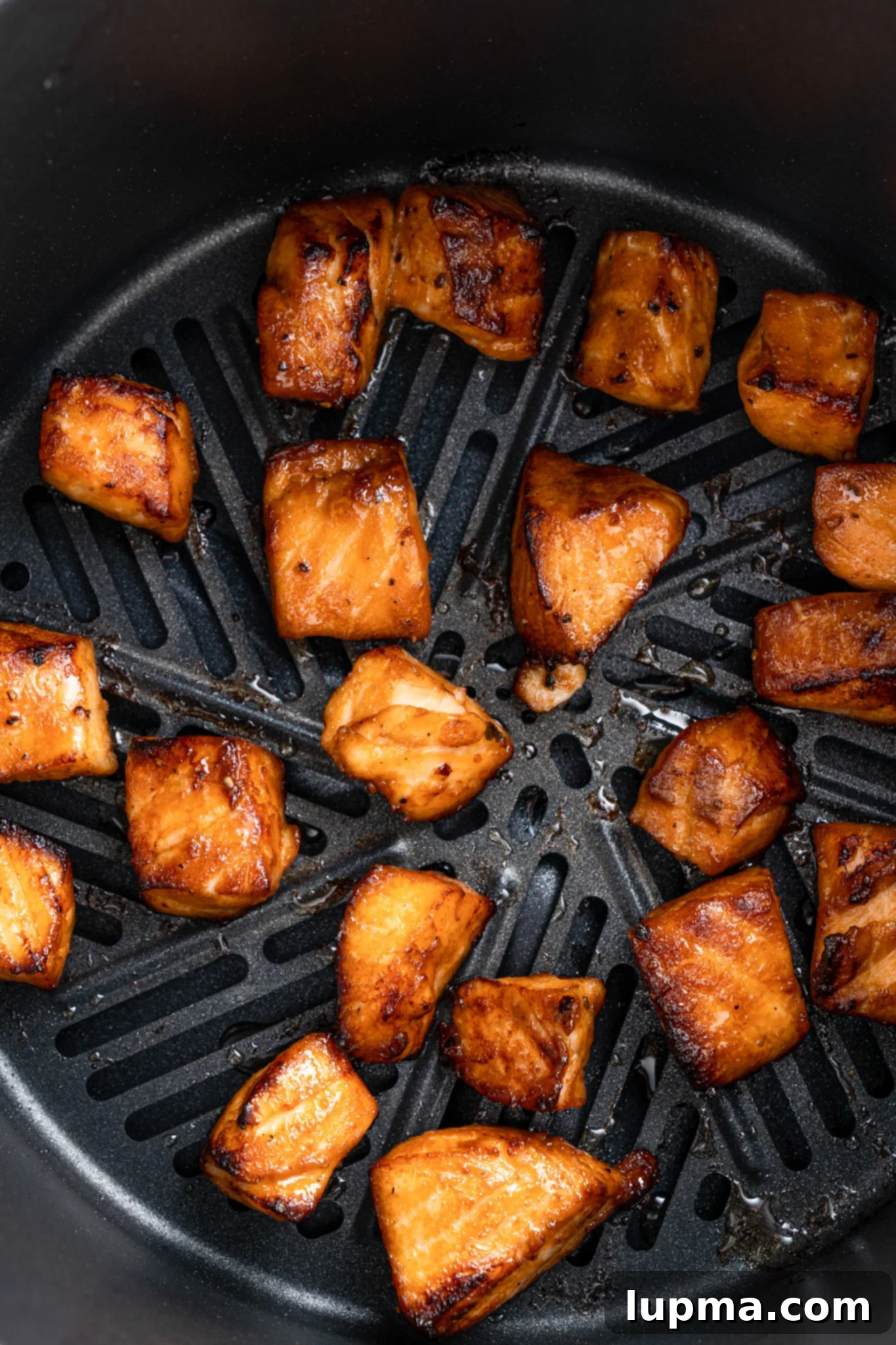 Teriyaki Salmon Bites: An Air Fryer Sensation 8 Chunks of glazed salmon are evenly spaced and cooked inside an air fryer basket.