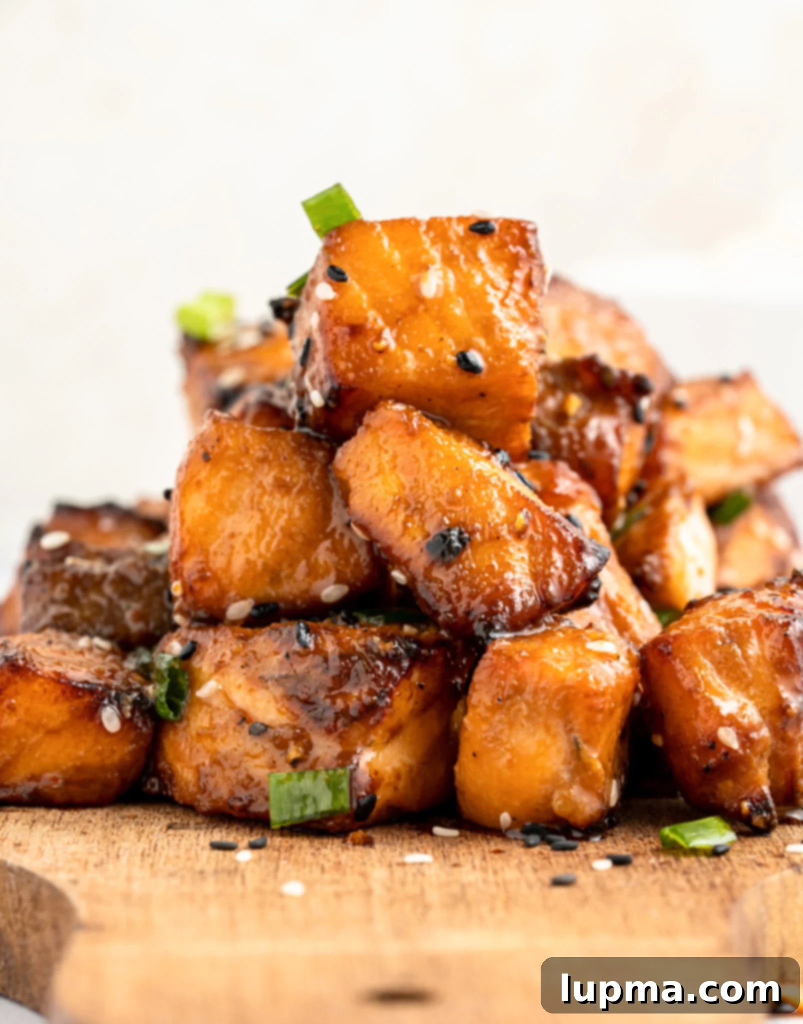 Teriyaki Salmon Bites: An Air Fryer Sensation 10 A stack of air fryer salmon bites garnished with sesame seeds and green onions on a wooden board.