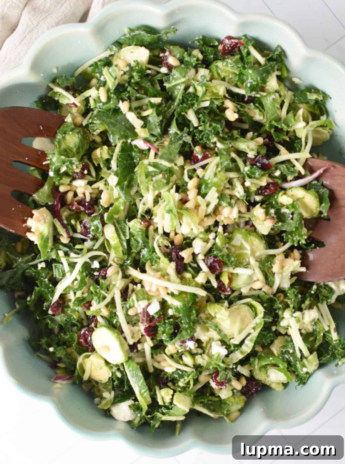Kale Brussels Sprout Salad in a bowl with wooden spoons, highlighting its fresh and vibrant ingredients