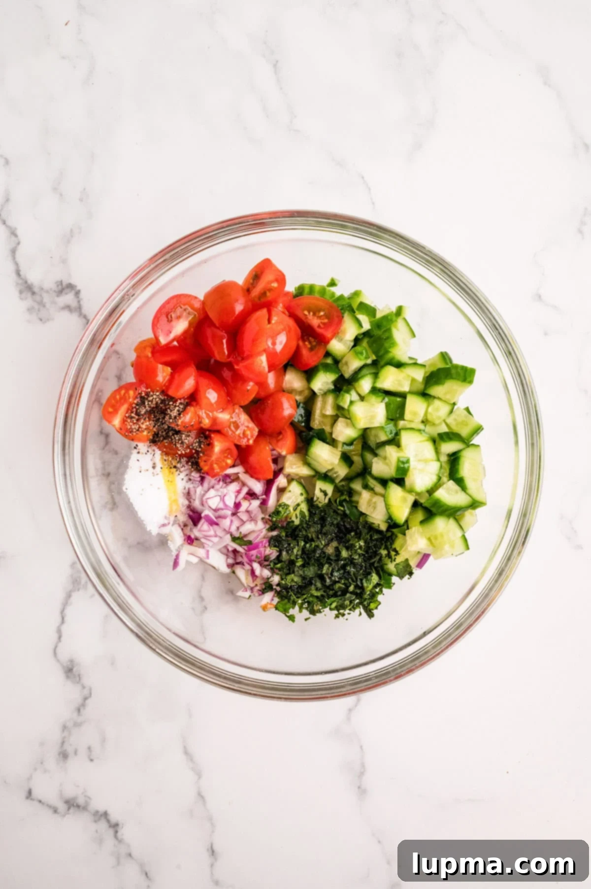 Fresh Mediterranean chicken topping ingredients mixed in a bowl, featuring cucumber, tomatoes, olives, and basil.