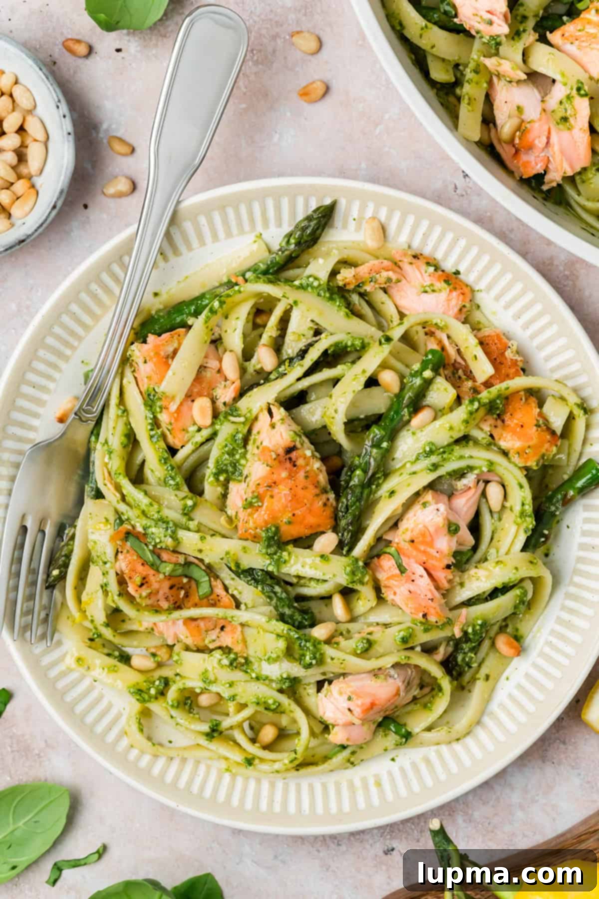 Close up of flaky pan seared salmon over pesto fettuccine with asparagus and Parmesan
