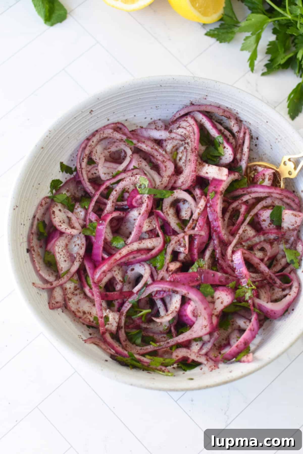 Overhead view of sumac onions in a small white bowl showing deep reddish purple color and fresh parsley