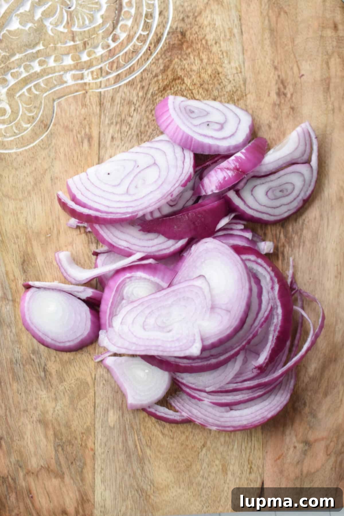 Thinly sliced red onion half moons on a cutting board for sumac onions recipe