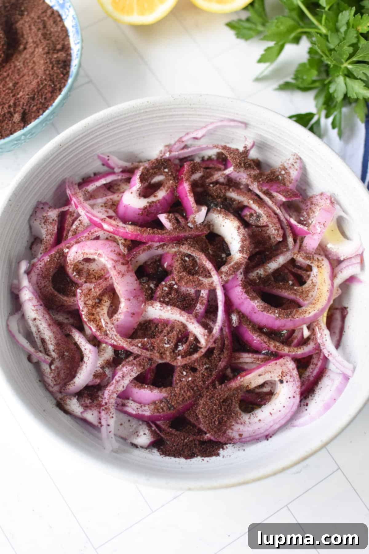Sliced red onions in a bowl with sumac, lemon juice, red wine vinegar 