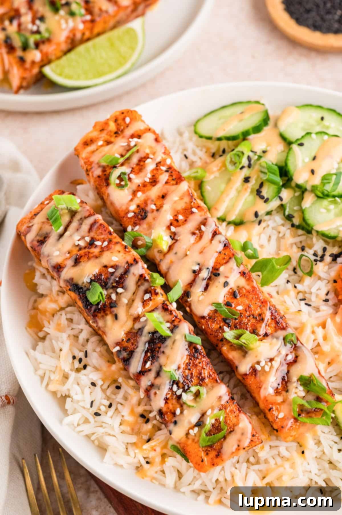 Bang bang salmon fillets topped with creamy sweet chili sauce served over rice with sliced cucumber and sesame seeds