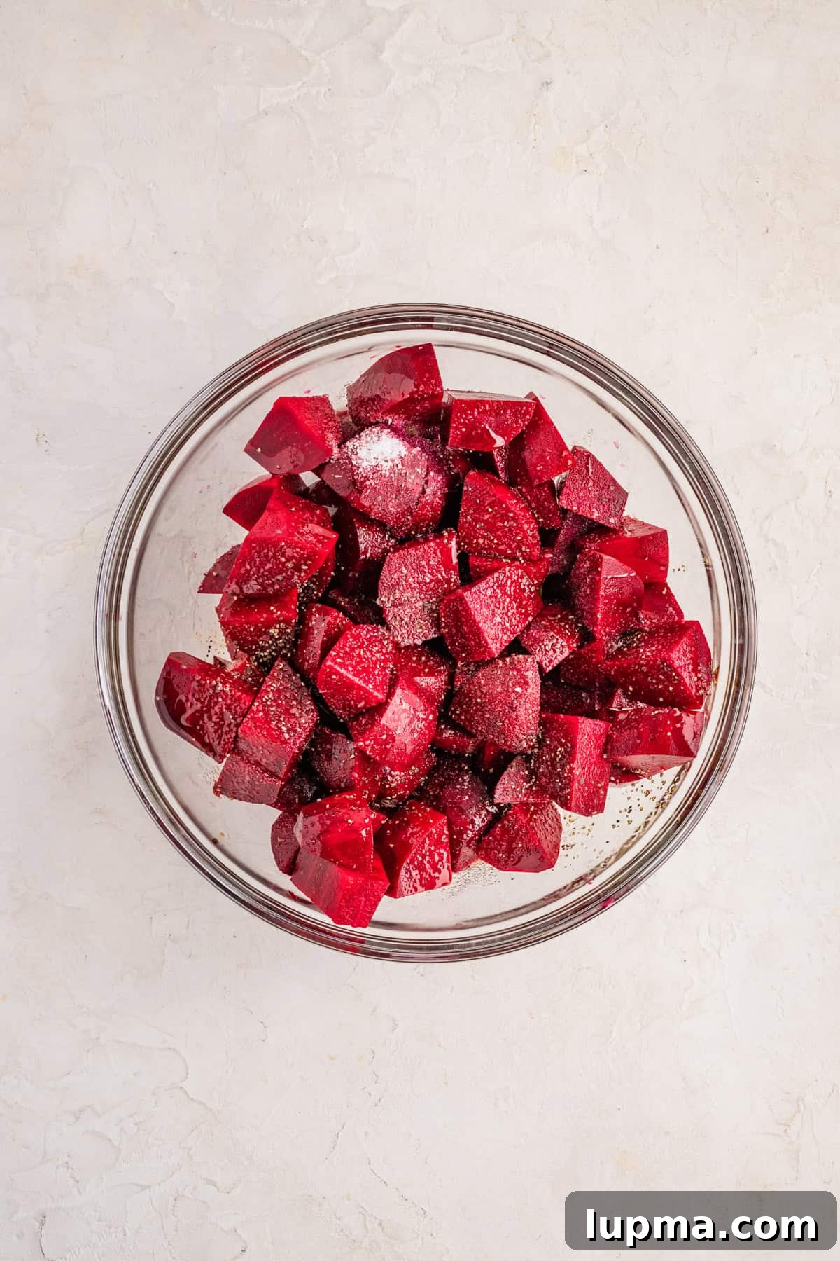 Raw beet cubes tossed in olive oil and balsamic vinegar in a large mixing bowl
