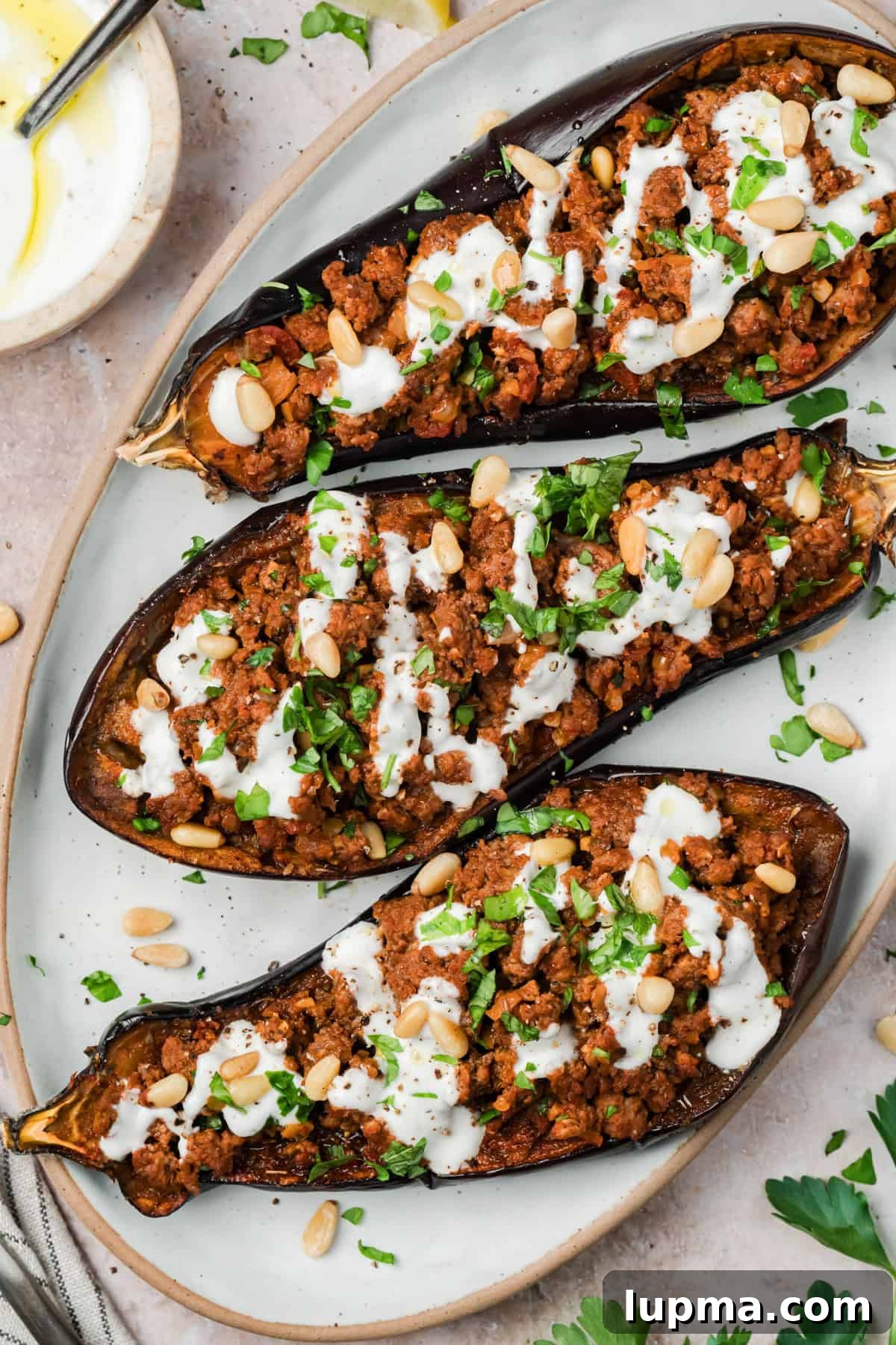 Mediterranean Stuffed Eggplant with Garlic Yogurt Sauce 2 Mediterranean stuffed eggplant with ground beef and garlic yogurt sauce on a white serving dish