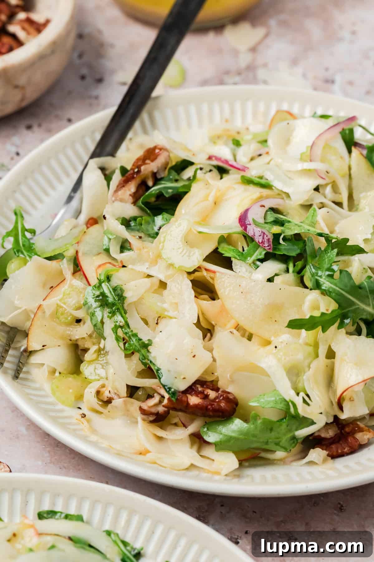Apple fennel salad with pecans and shaved Parmesan in a white bowl
