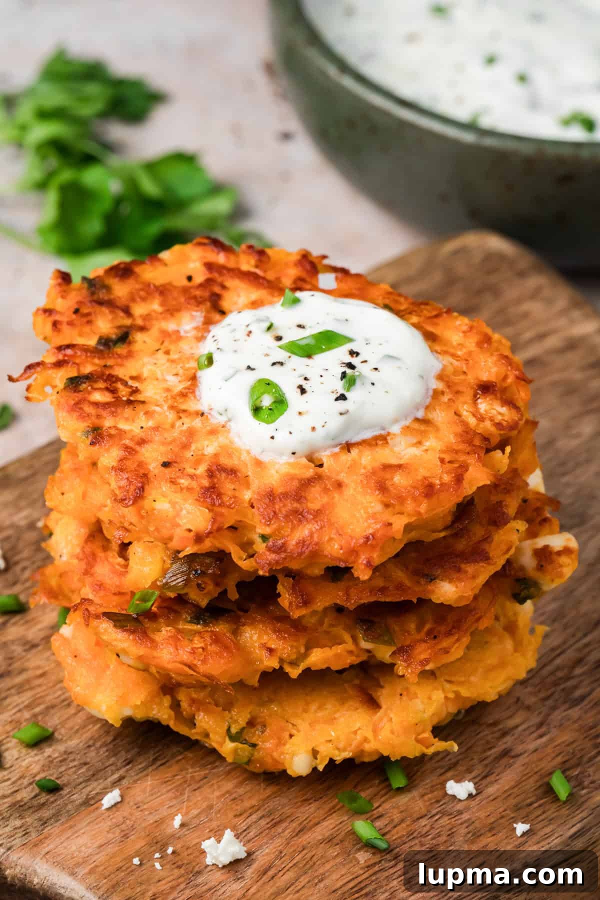 Crispy sweet potato fritters with feta stacked on a plate with lemon herb yogurt sauce