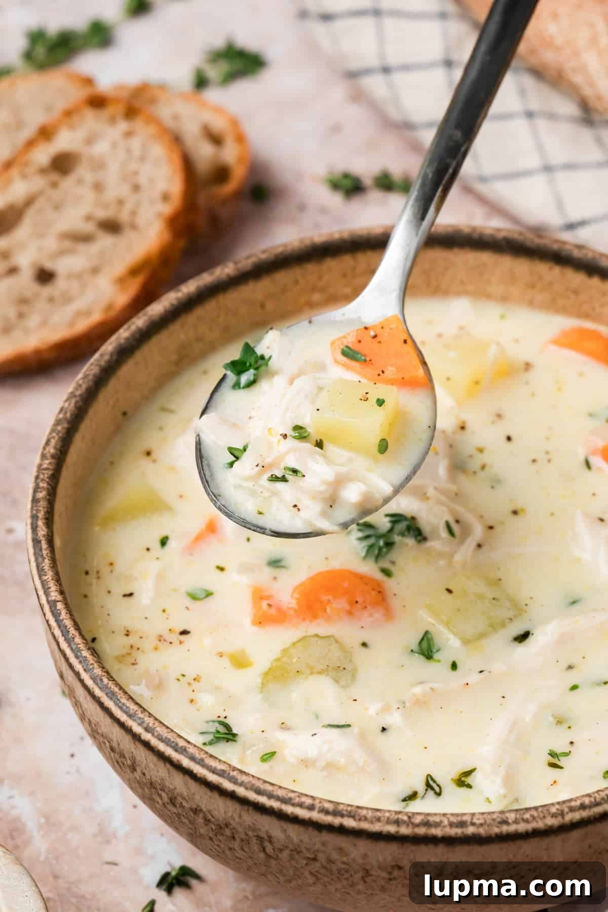 Creamy chicken and potato soup in a bowl with a spoon lifting a bite showing shredded chicken and potatoes