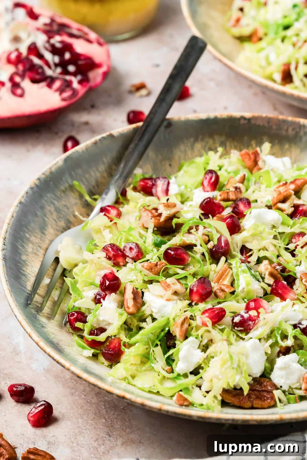 Shaved Brussels sprouts salad with pomegranate arils, pecans, and goat cheese in a serving bowl