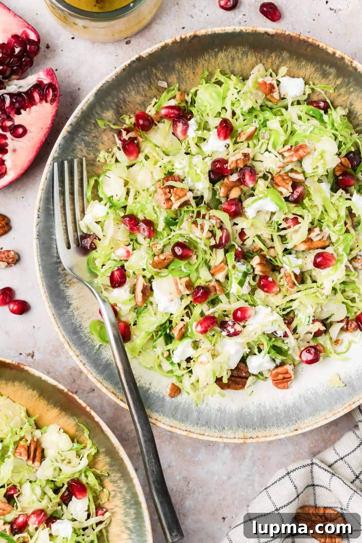 Shaved Brussels sprouts salad with pomegranate, pecans, and goat cheese on a table with scattered pomegranate arils